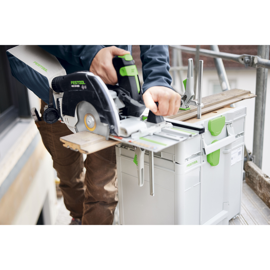 Person operating a Festool circular saw mounted on an interlocking SYS3-MFT M 112 modular work surface with tool storage on a construction site.