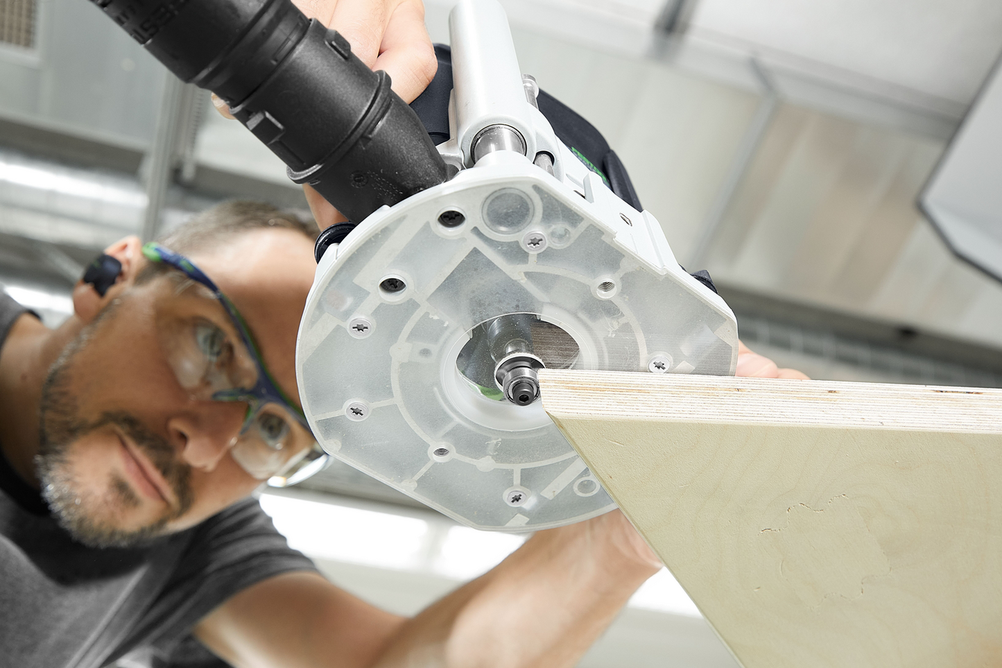 Man using Festool router for precise edge trimming on light wood panel in a well-lit workshop setting
