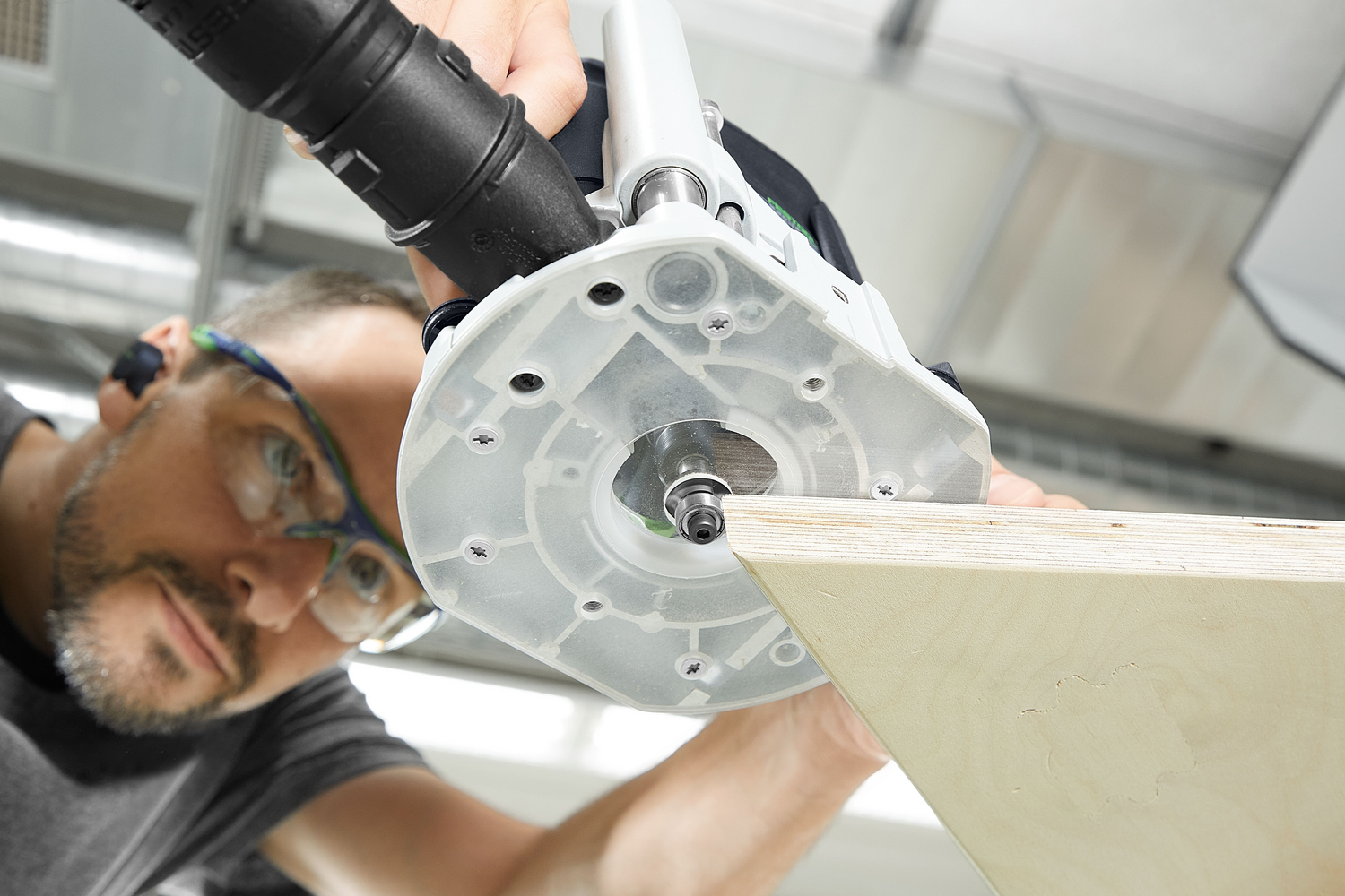 Man using Festool router for precise edge trimming on light wood panel in a well-lit workshop setting