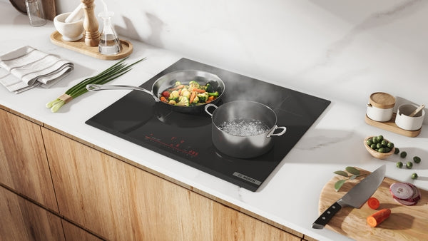 Black 24-inch induction cooktop with two pots boiling and stir-frying vegetables on modern kitchen countertop