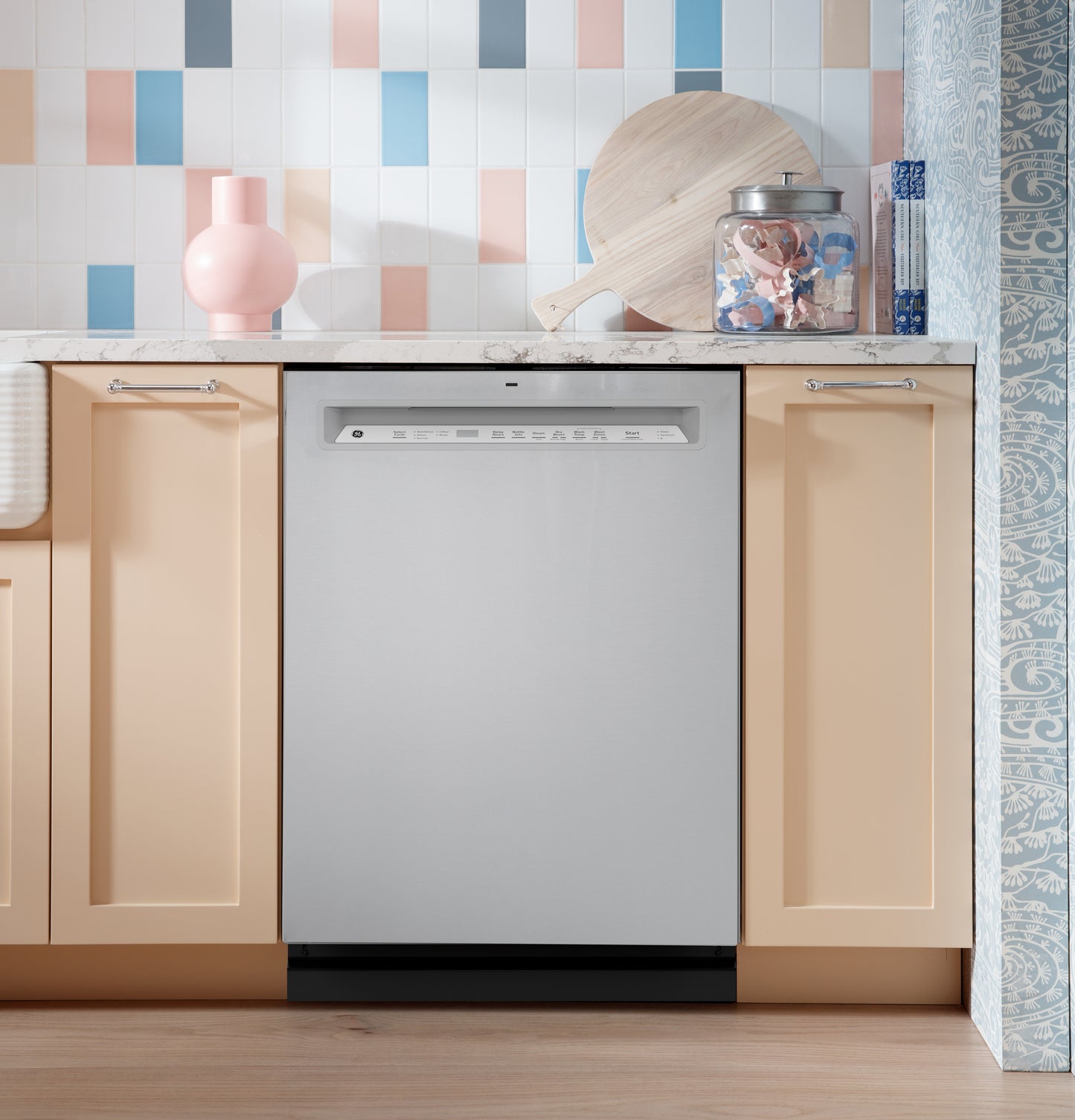 Front control stainless steel dishwasher integrated into kitchen cabinetry with pastel backsplash and countertop decor