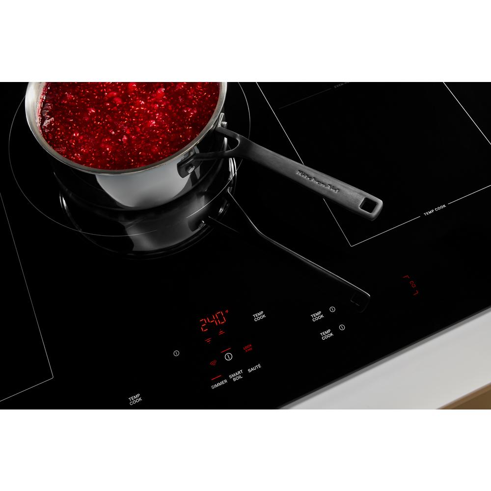 Black induction cooktop with digital controls heating a stainless steel pot of simmering red sauce in kitchen appliances setting