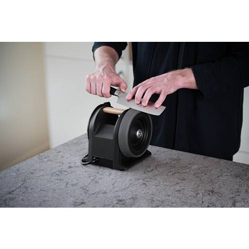 Person sharpening a kitchen knife with a carbon black sharpener featuring a wooden handle on gray countertop