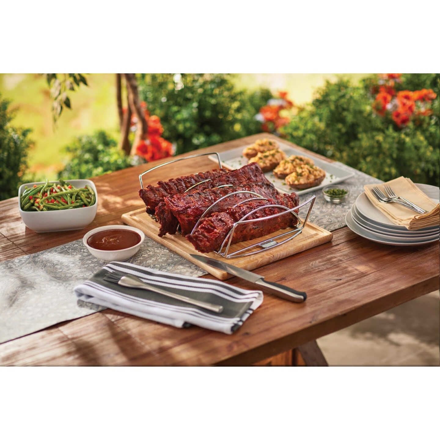 Outdoor dining table set with ribs in stainless steel rib rack, side dishes, and barbecue sauce in Grill Accessories collection