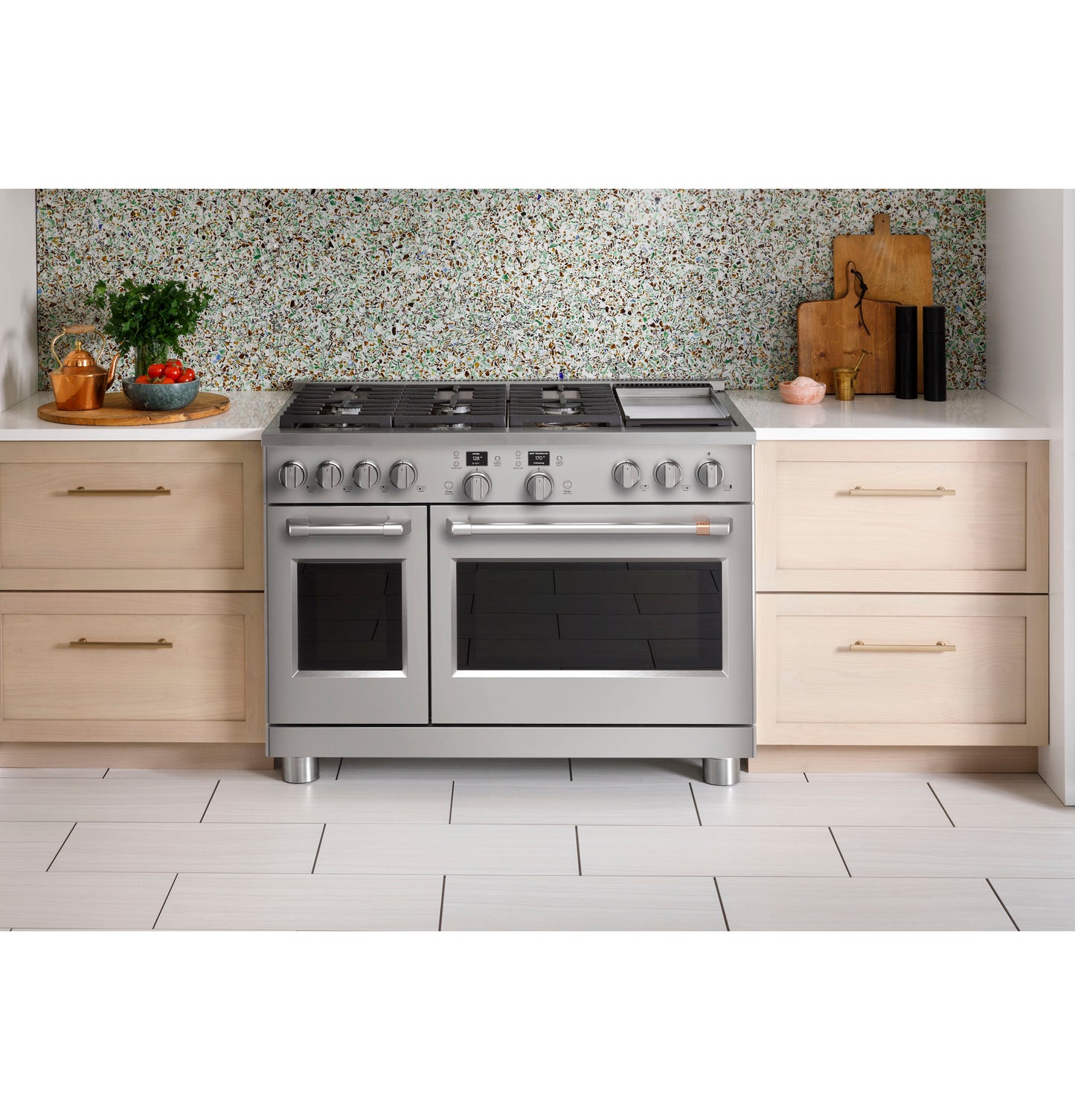 Stainless steel dual-fuel range with six burners, griddle, and double ovens in modern kitchen setting