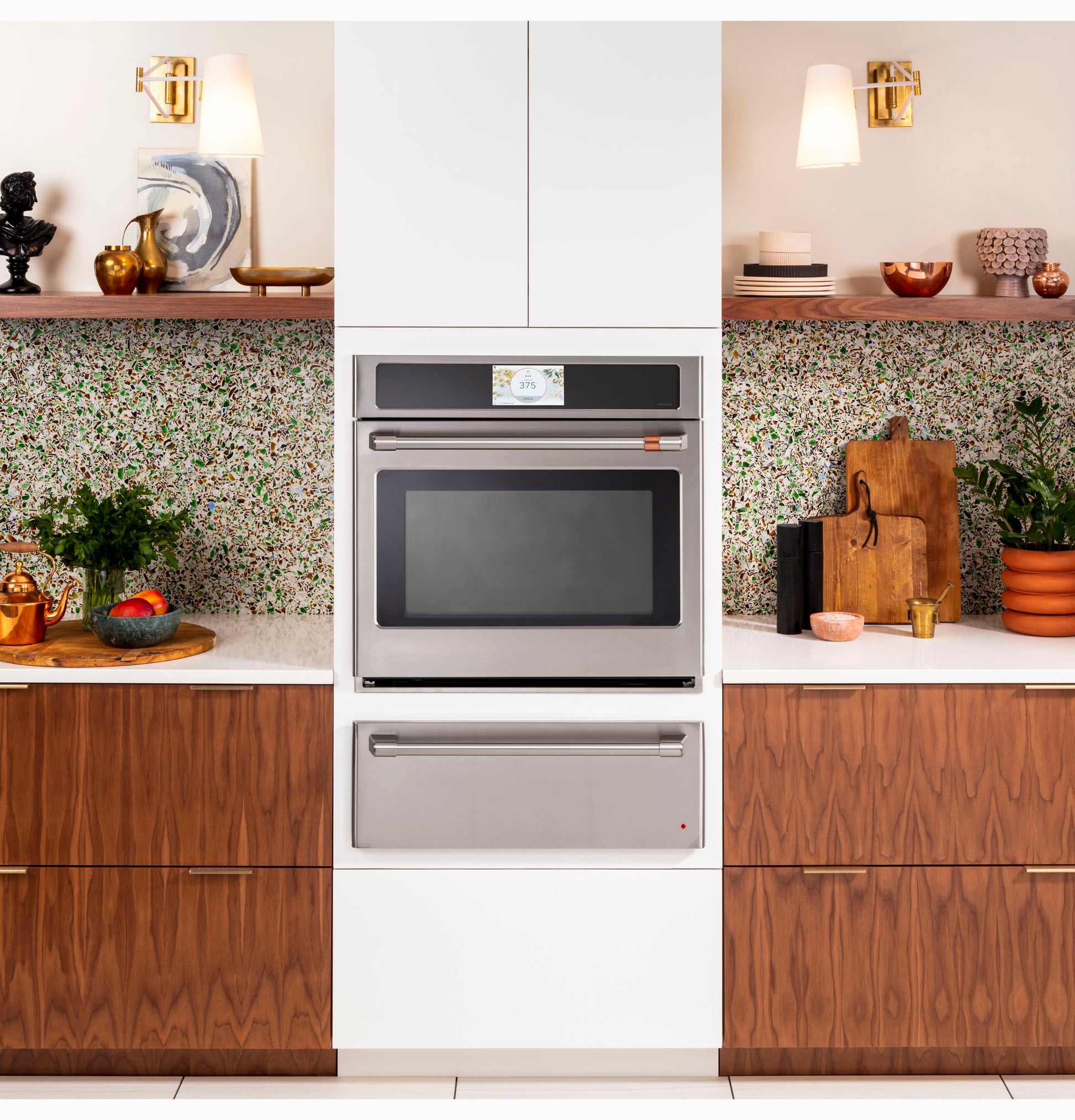 Built-in stainless steel warming drawer below wall oven in modern kitchen with wood cabinets and terrazzo backsplash