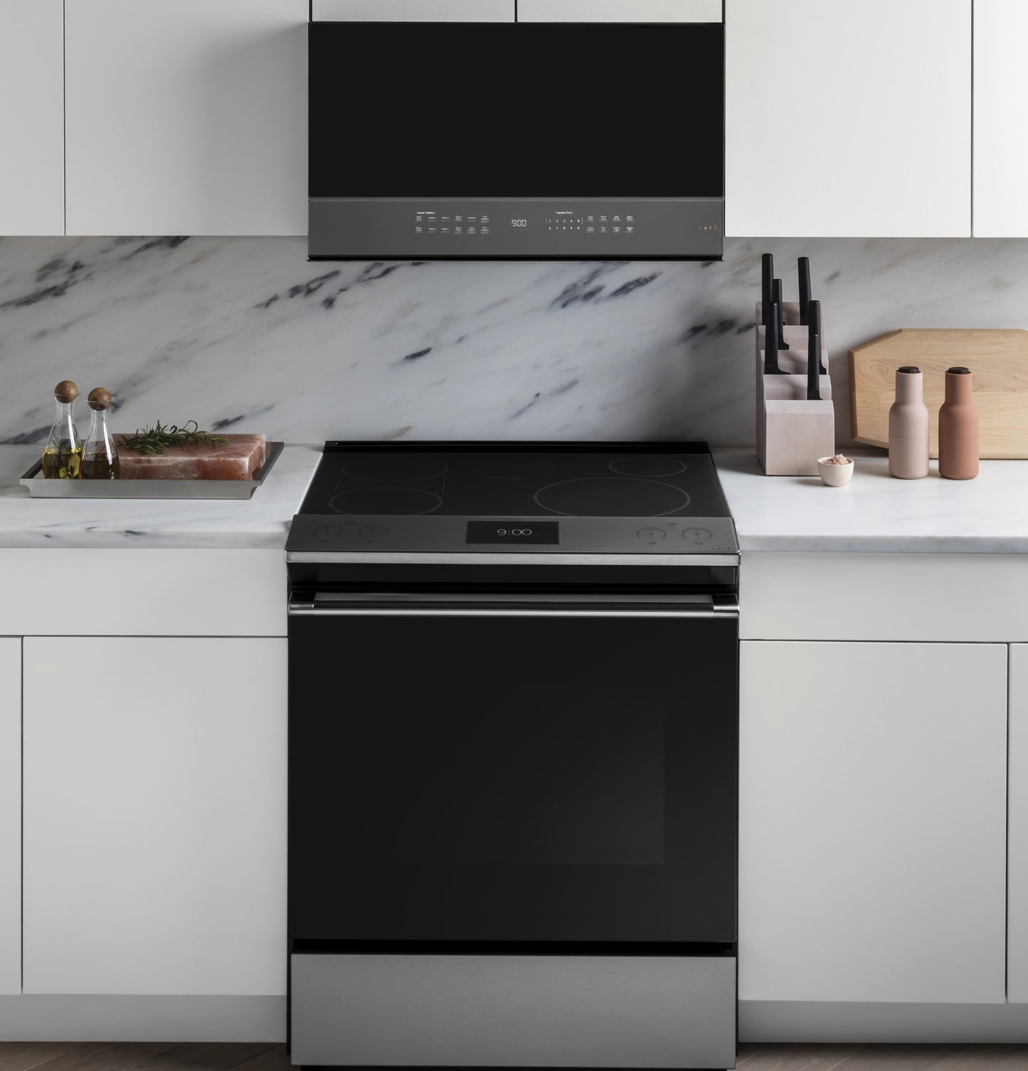 Modern kitchen with black over-the-range microwave and black electric range surrounded by white cabinets and marble backsplash