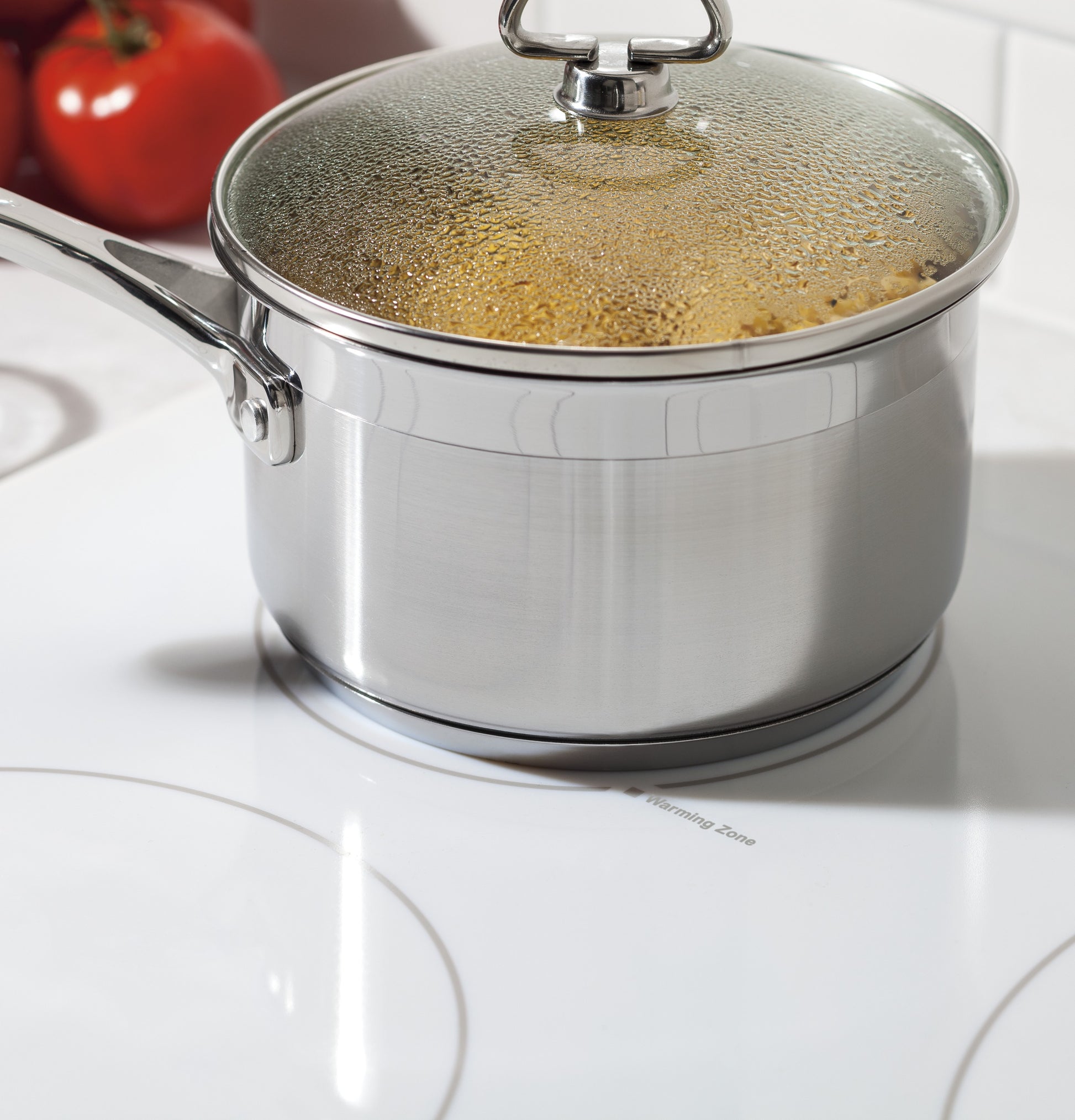 Stainless steel saucepan with glass lid steaming on white electric cooktop in kitchen and home improvement setting