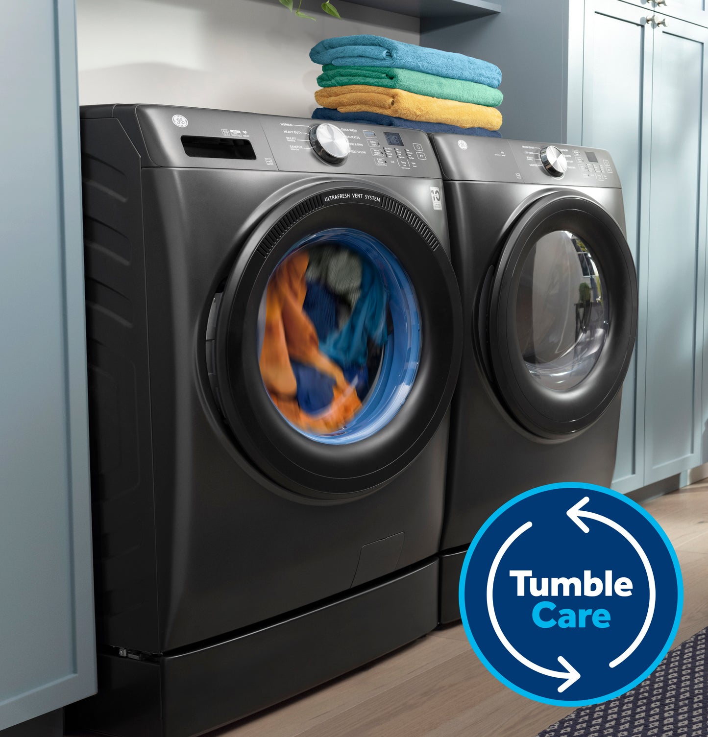Dark gray smart front load washer with clothes tumbling inside and matching dryer in laundry room setting