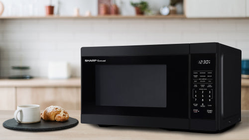 Sleek black countertop microwave oven with digital display, set on kitchen counter next to white cup and croissant plate