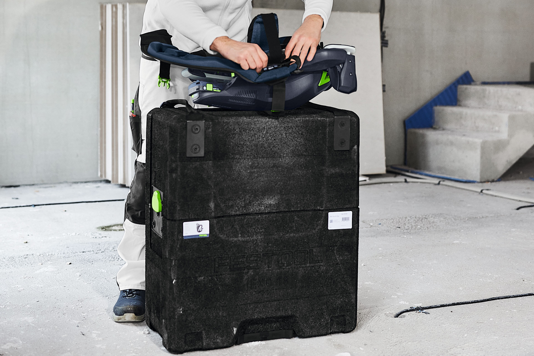 Person adjusting black and green ergonomic exoskeleton on sturdy case in unfinished room for power tool accessories
