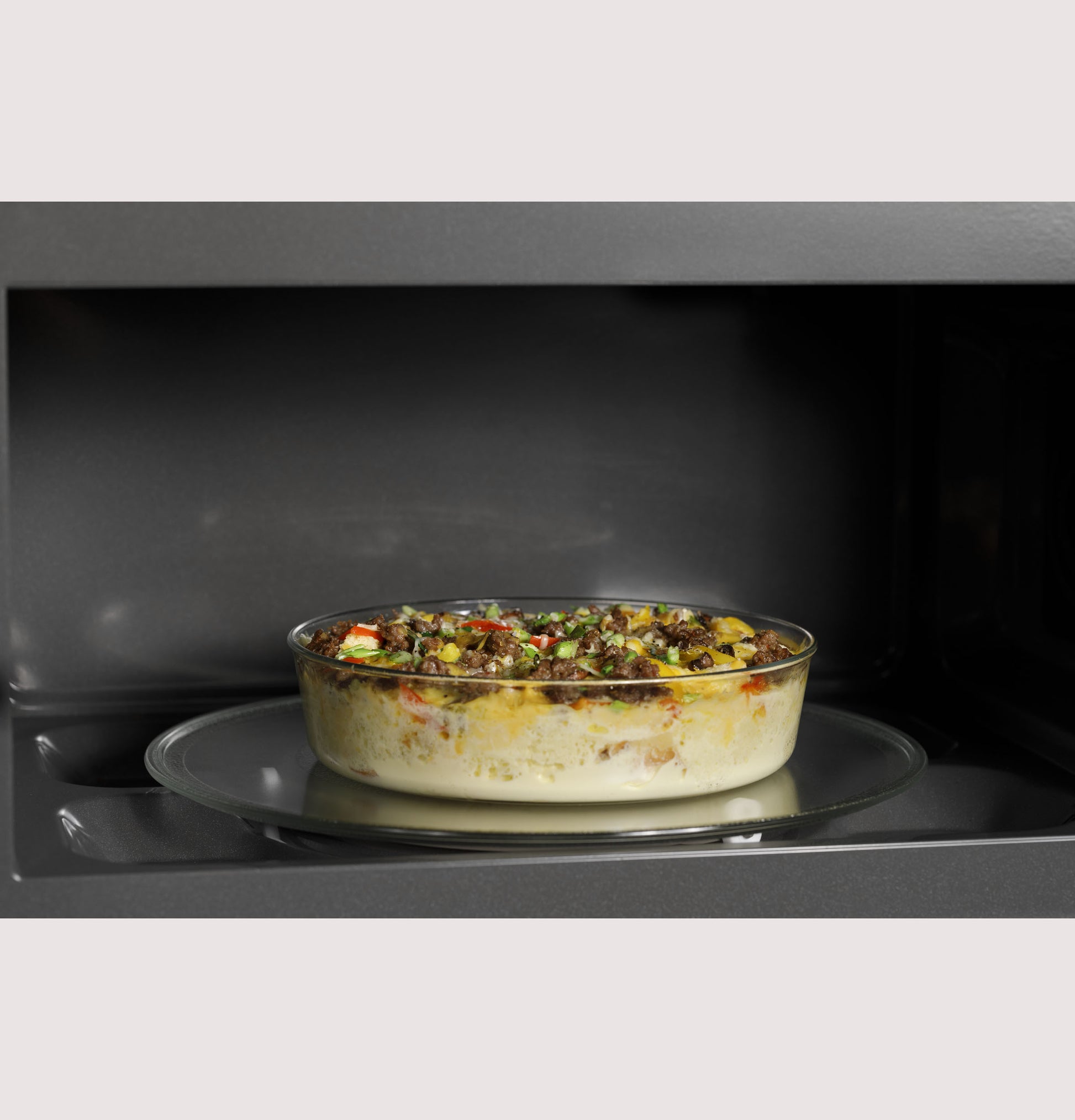 Glass dish with casserole cooking inside the interior of an over-the-range microwave oven from kitchen appliances collection