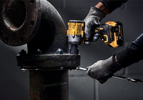 Gloved hand using DEWALT cordless impact wrench on large rusted metal pipe for tools and home improvement tasks
