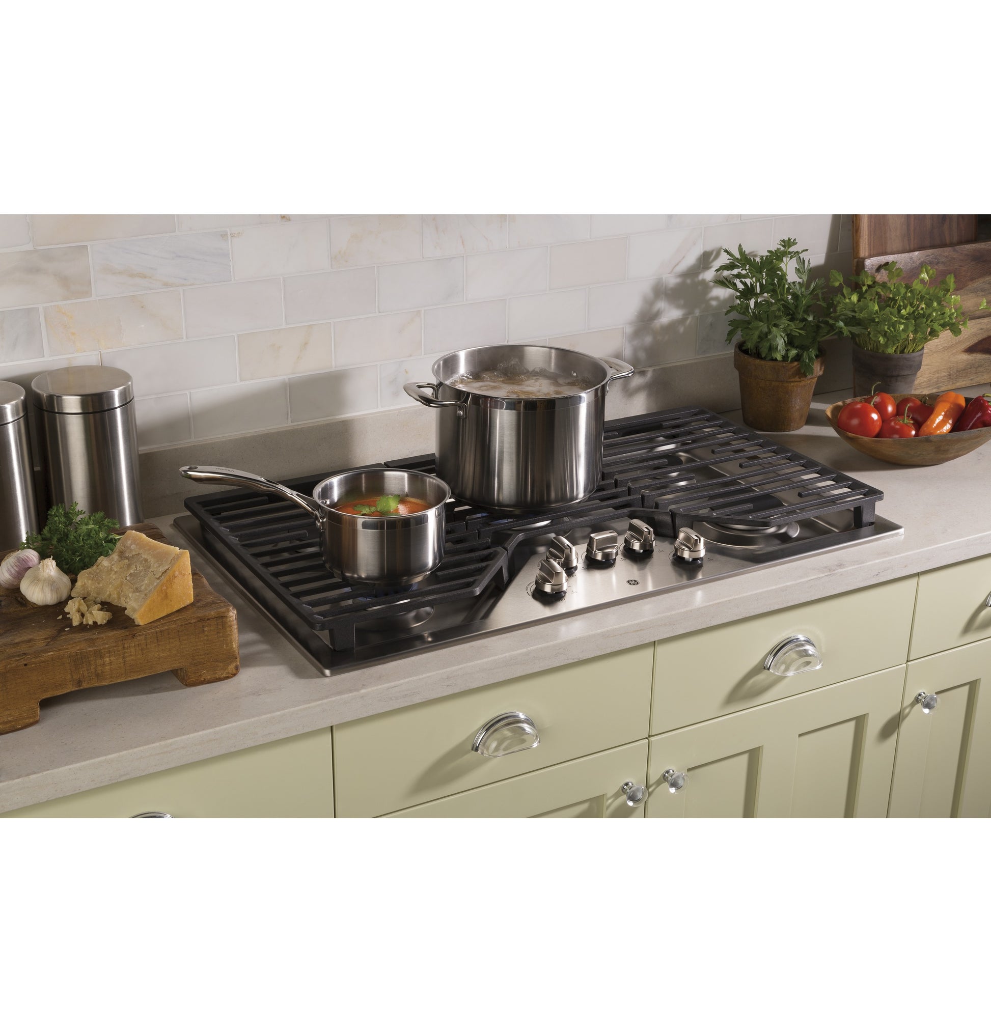 Built-in gas cooktop with five burners and black dishwasher-safe grates installed on light green cabinetry in kitchen setting