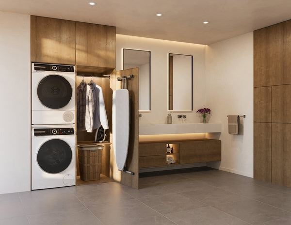 Stacked compact white washer and dryer in modern laundry room with wood cabinetry and built-in storage shelves.