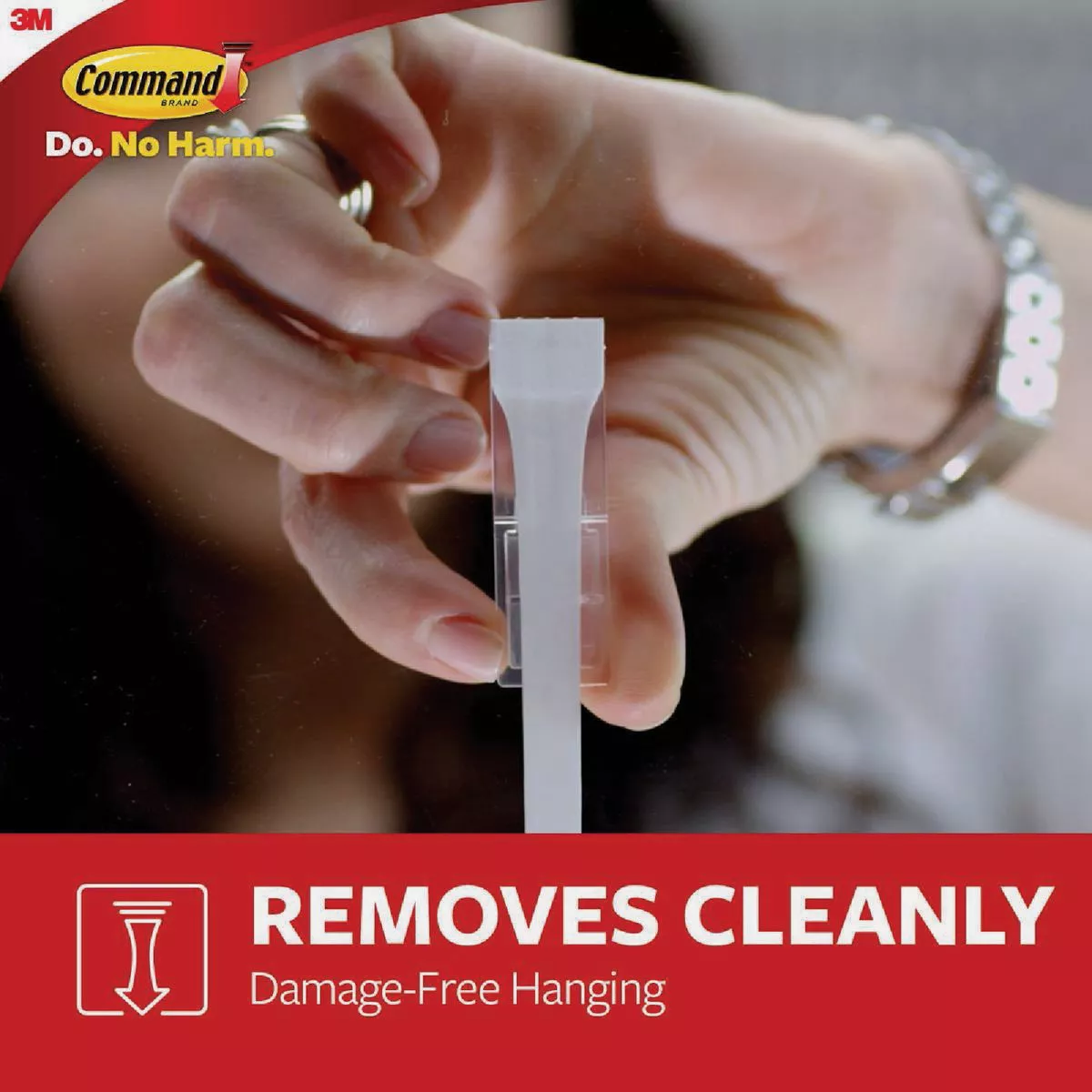 Hand holding white adhesive strip for damage-free hanging in hardware and fasteners category under $50