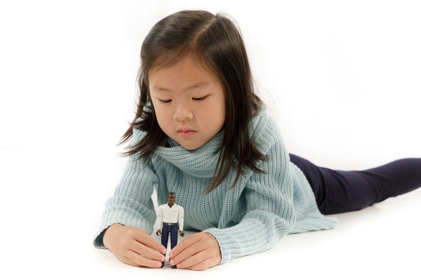 Child lying down playing with a dark-skinned male toy figure wearing a white shirt and dark blue jeans