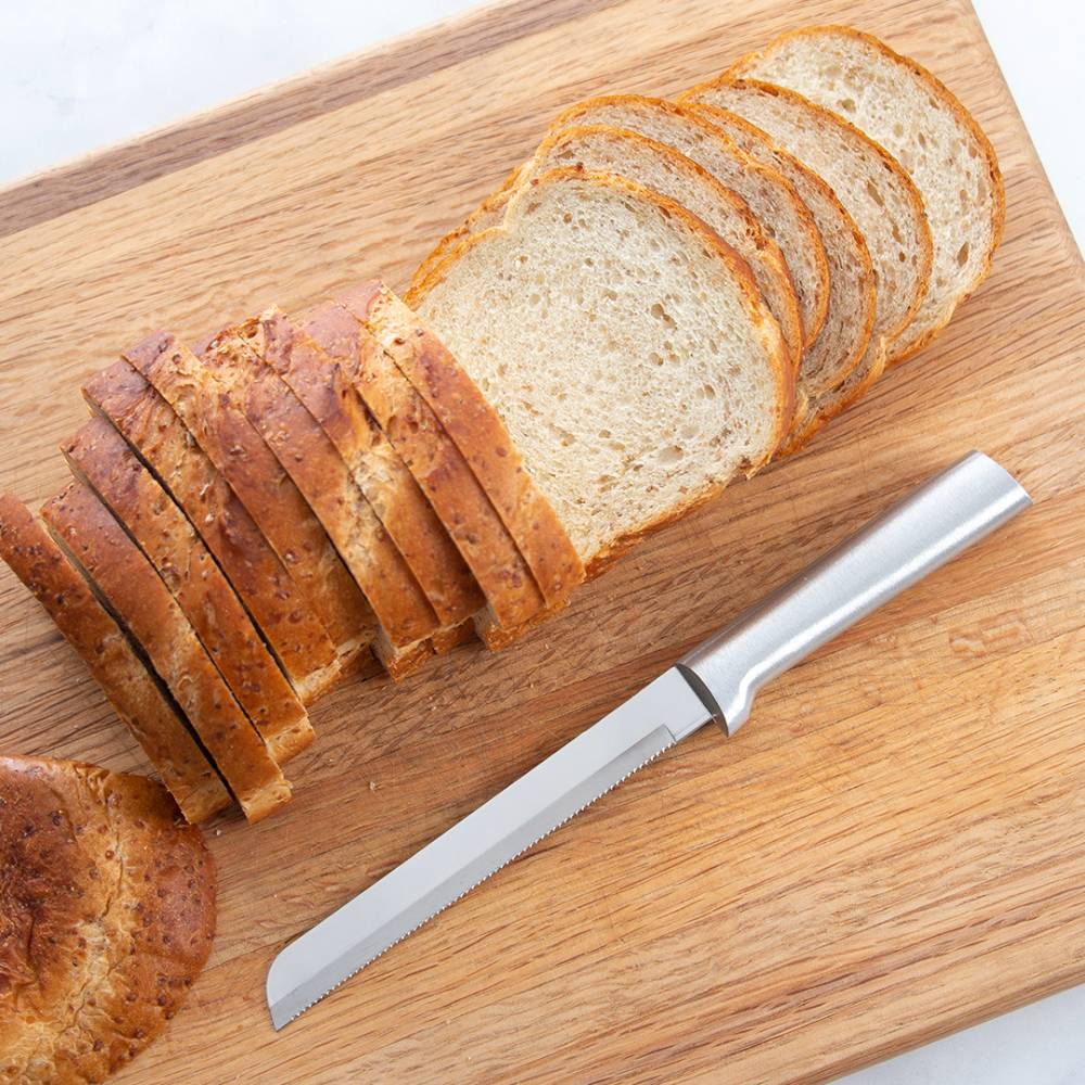 Sharp stainless steel serrated knife with smooth handle beside sliced multigrain and white bread on wooden board