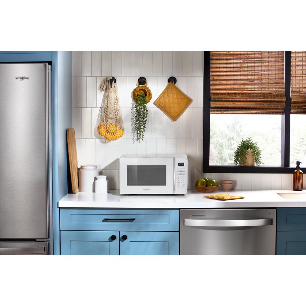 White countertop microwave with digital touch controls on blue kitchen cabinet countertop near stainless appliances and window