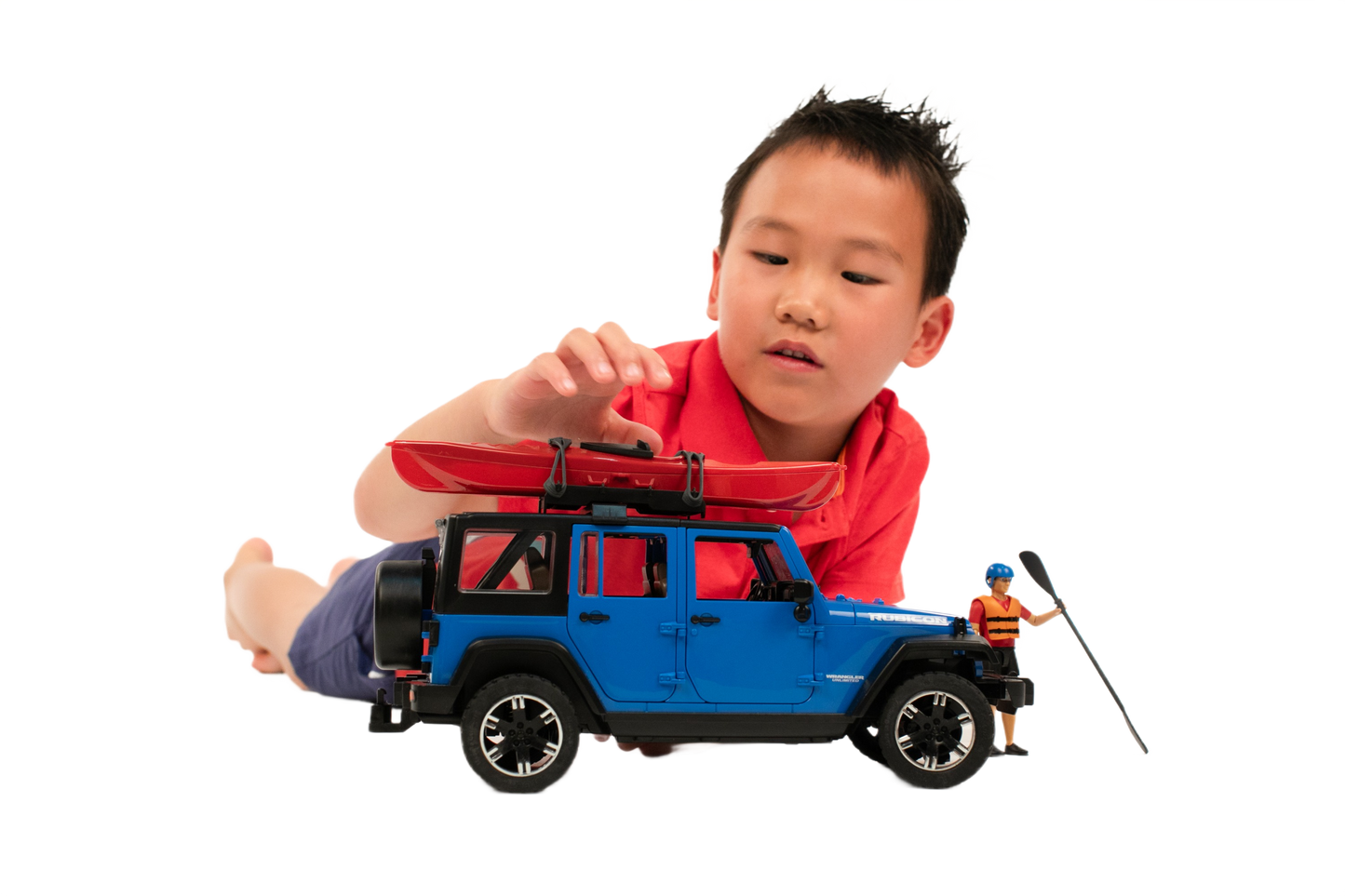 Child in red shirt playing with blue toy Jeep Wrangler Rubicon featuring red kayak and action figure with fishing rod