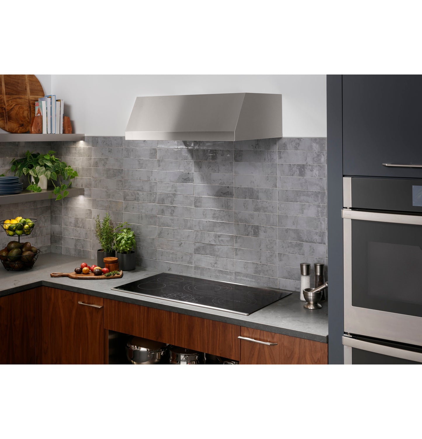 Modern kitchen setup with built-in electric cooktop, stainless steel range hood, and gray tiled backsplash.