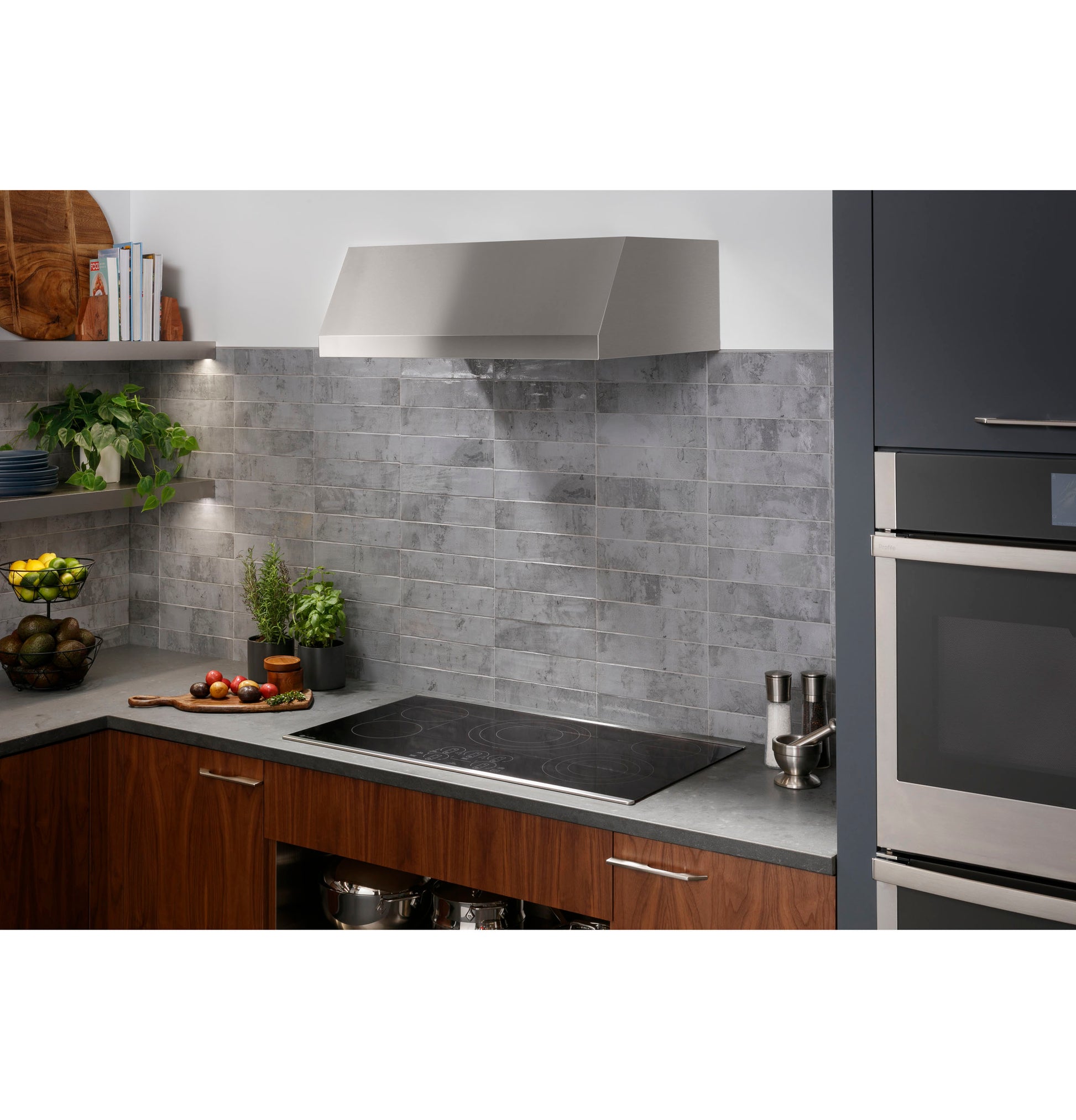 Modern kitchen setup with built-in electric cooktop, stainless steel range hood, and gray tiled backsplash.
