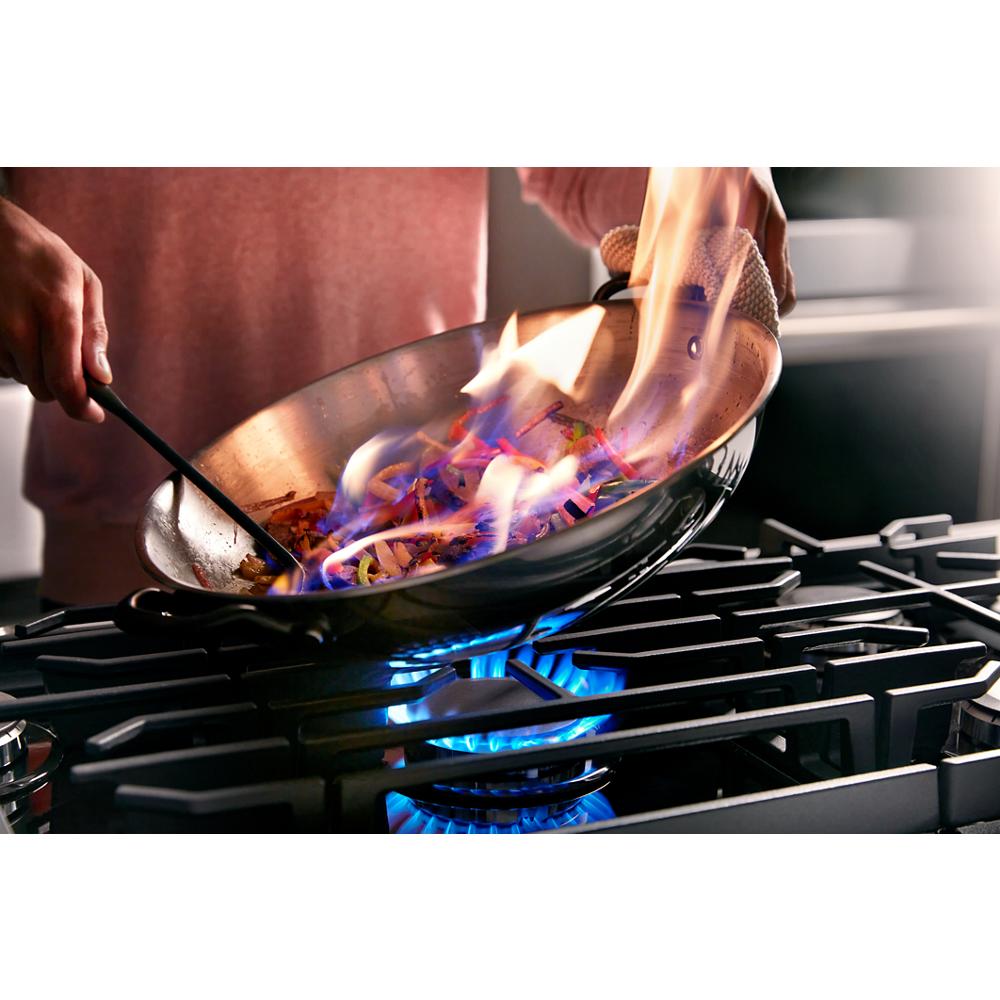 Copper wok with visible flames over blue burner on black gas cooktop in home improvement and kitchenware setting