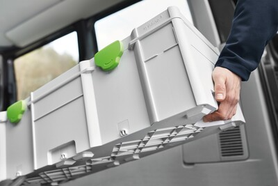 Person carrying large gray modular storage box with green latches for workshop or jobsite tool organization