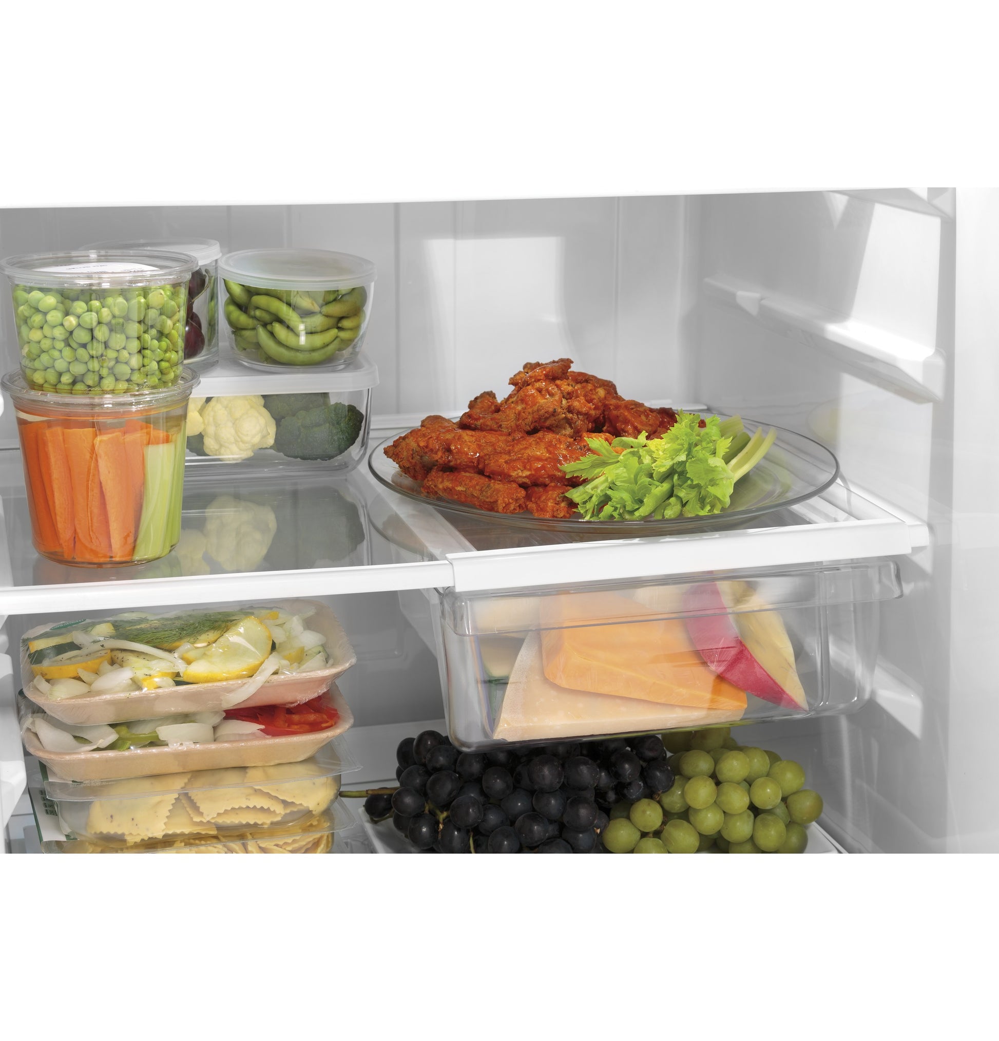 Open refrigerator interior showing organized fresh vegetables, prepared meals, and fruits in clear containers for kitchen appliances collection
