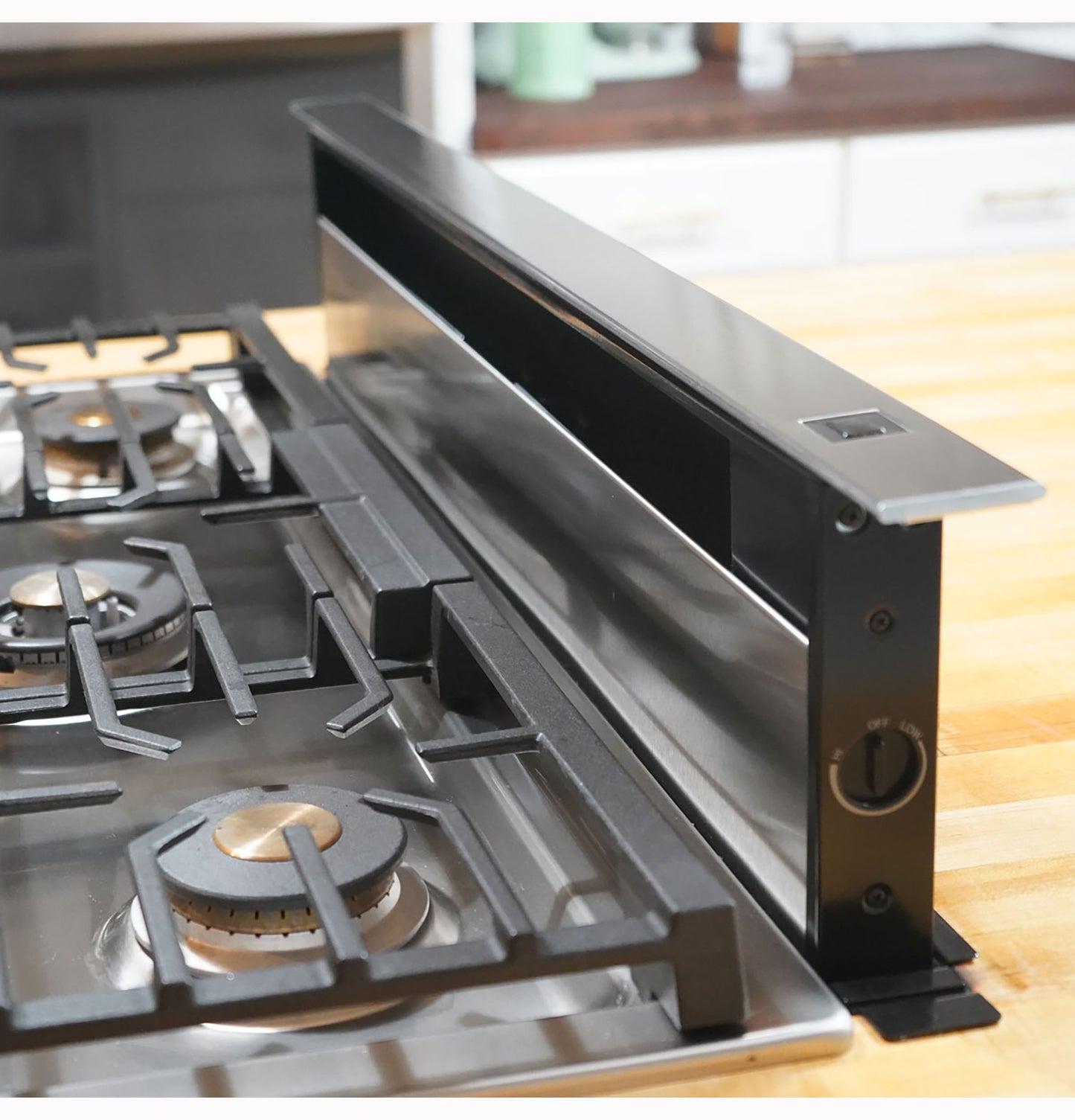 Black telescopic downdraft vent system installed behind gas cooktop for ventilation in kitchen appliances and range hoods collections