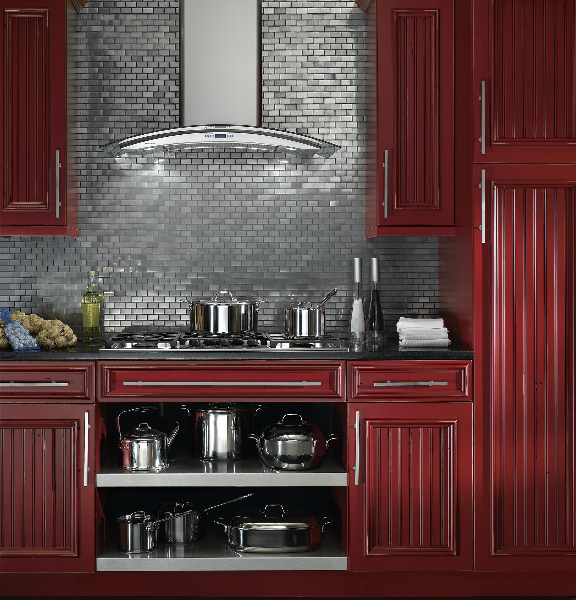 Curved glass canopy wall-mounted hood above stovetop with stainless steel cookware in kitchen appliances setting