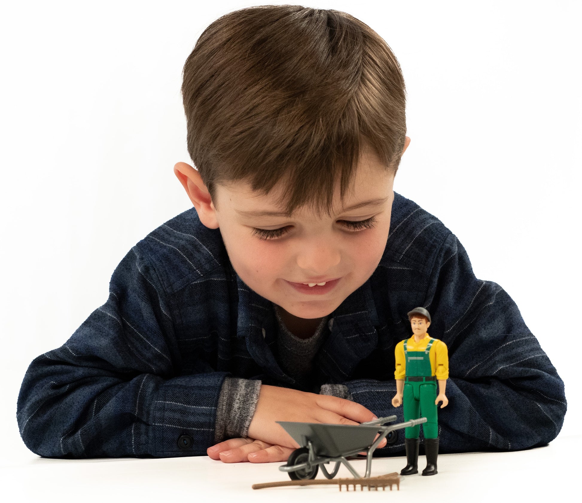 Young child playing with Bruder Toys gardener figure dressed in yellow and green with wheelbarrow and rake in toys collection