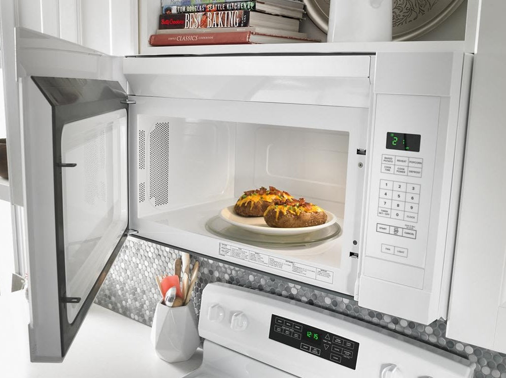 White over-the-range microwave with digital controls and baked potatoes cooking inside in kitchen appliances collection