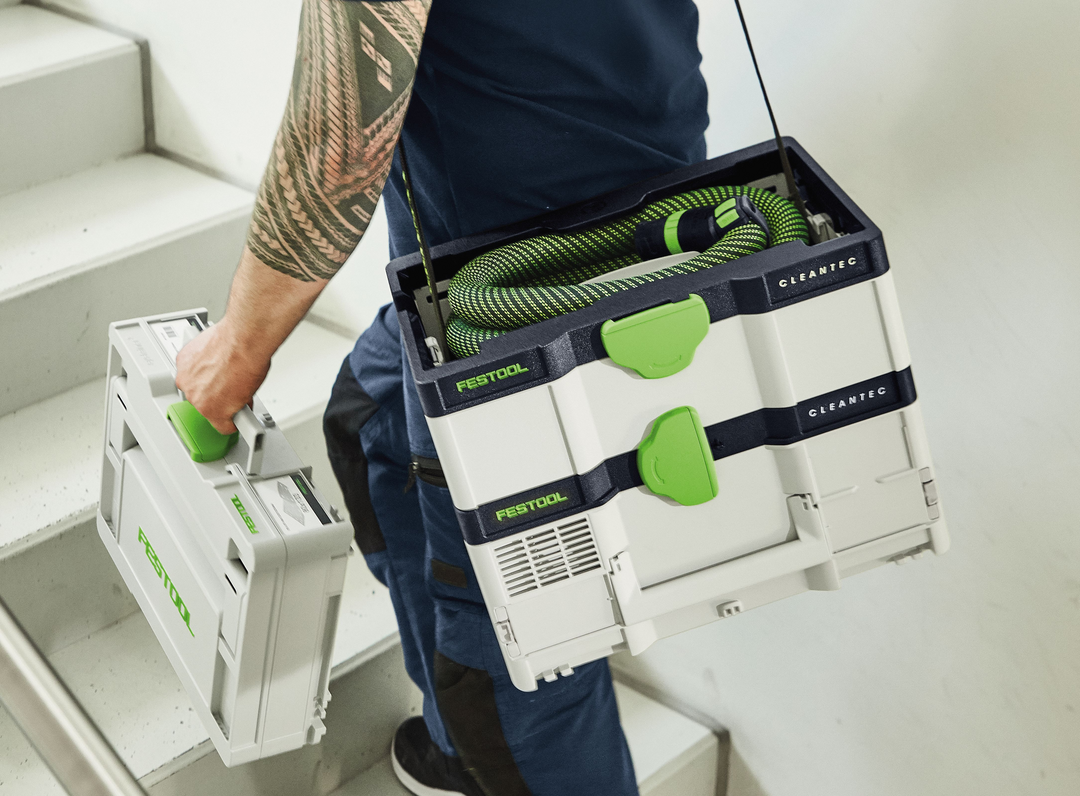 Person carrying Festool cordless HEPA dust extractor and matching compact tool case up stairs for woodworking tasks