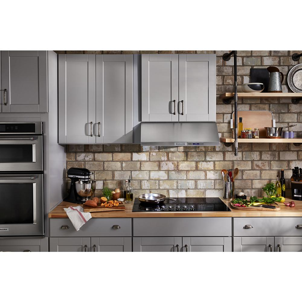 Modern kitchen with gray cabinetry, brick backsplash, wood countertops, and a sleek black electric cooktop with knobs