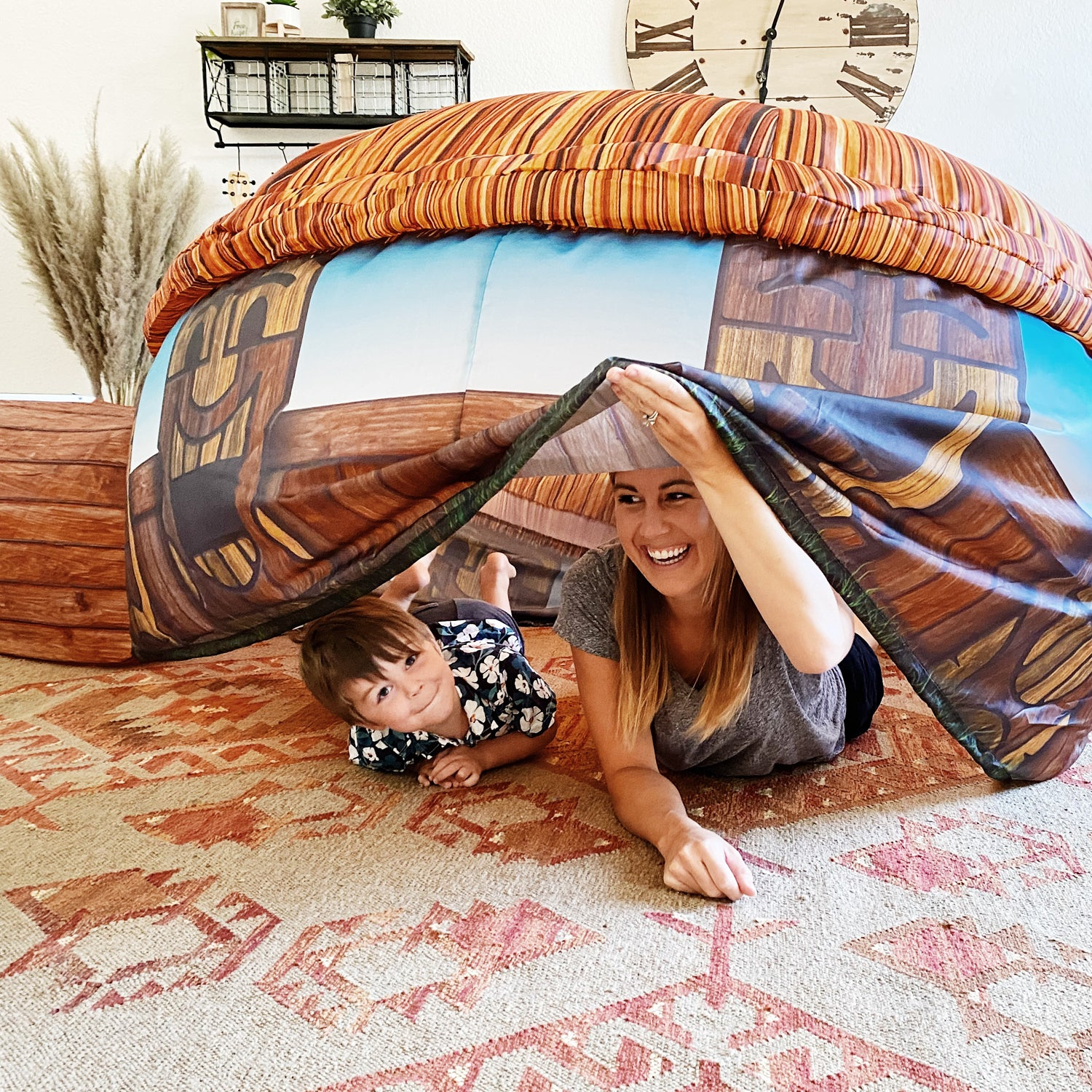 Woman and child playing inside colorful inflatable Tiki Hut themed indoor play structure on patterned rug