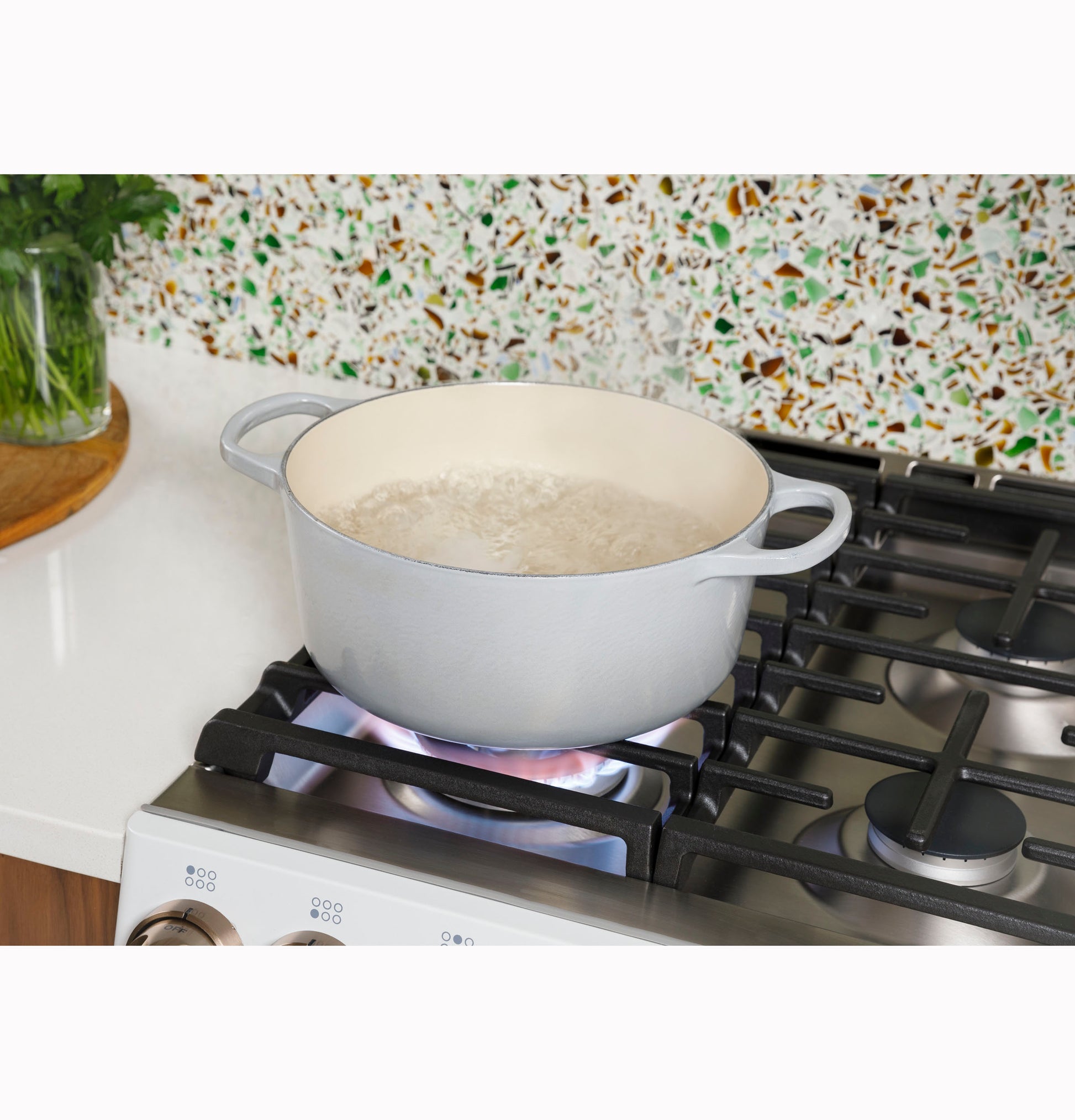 Light gray cast iron pot boiling water on a stainless steel gas cooktop in a modern kitchen setting