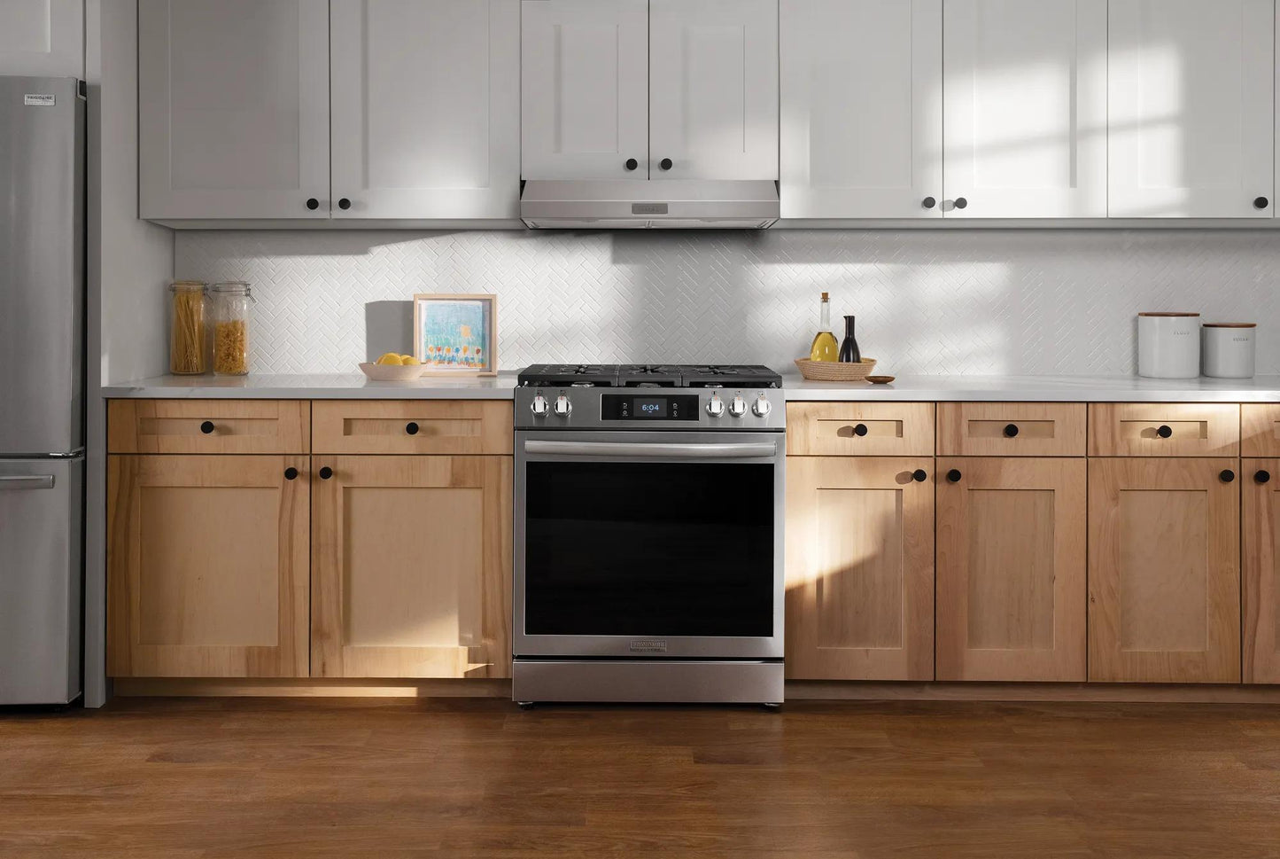 Modern kitchen with stainless steel range, light wood lower cabinets, white upper cabinets, and undercabinet vent hood