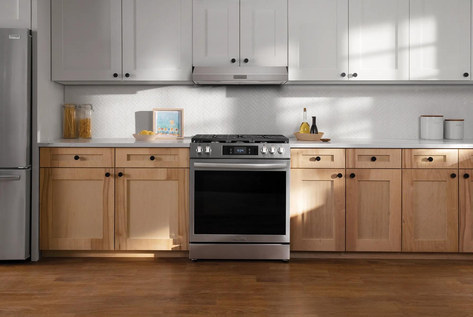 Modern kitchen with stainless steel range, light wood lower cabinets, white upper cabinets, and undercabinet vent hood