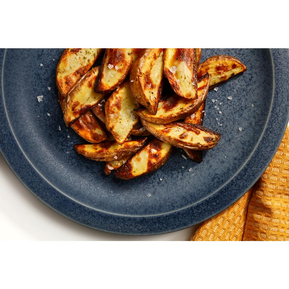 Crispy air fried potato wedges sprinkled with coarse salt served on a dark blue plate with a yellow napkin nearby