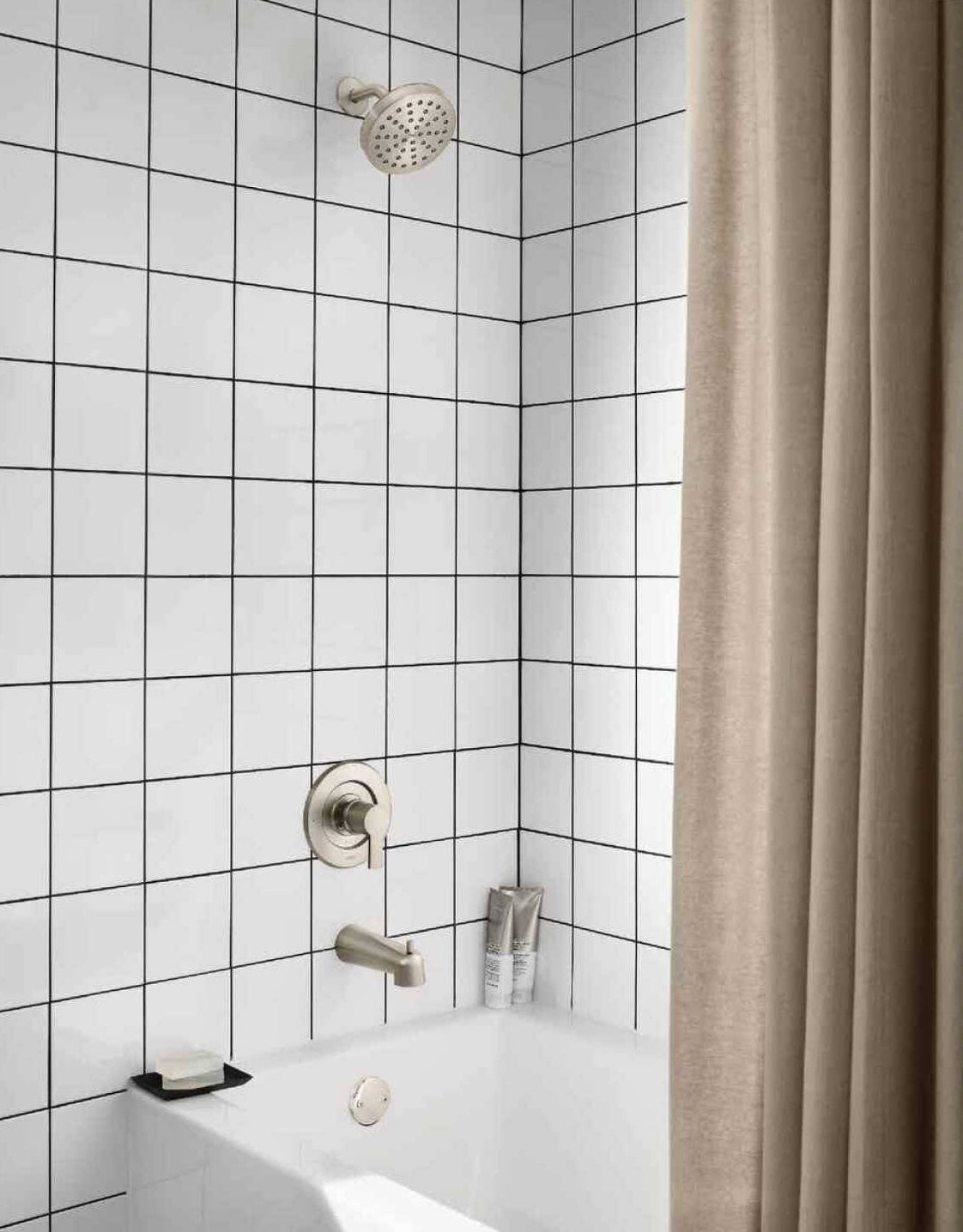 Modern brushed nickel single-handle tub and shower trim installed in white tiled bathroom setting with beige shower curtain