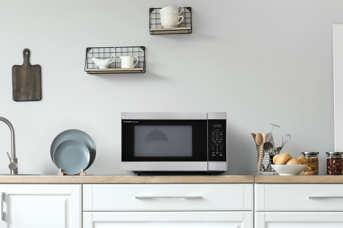 Stainless steel countertop microwave with digital control panel in modern kitchen featuring white cabinetry and wooden accents