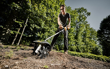 Gardener using DEWALT cultivator attachment with steel tines on soil in outdoor setting from Dewalt Outdoor Power Tools collection