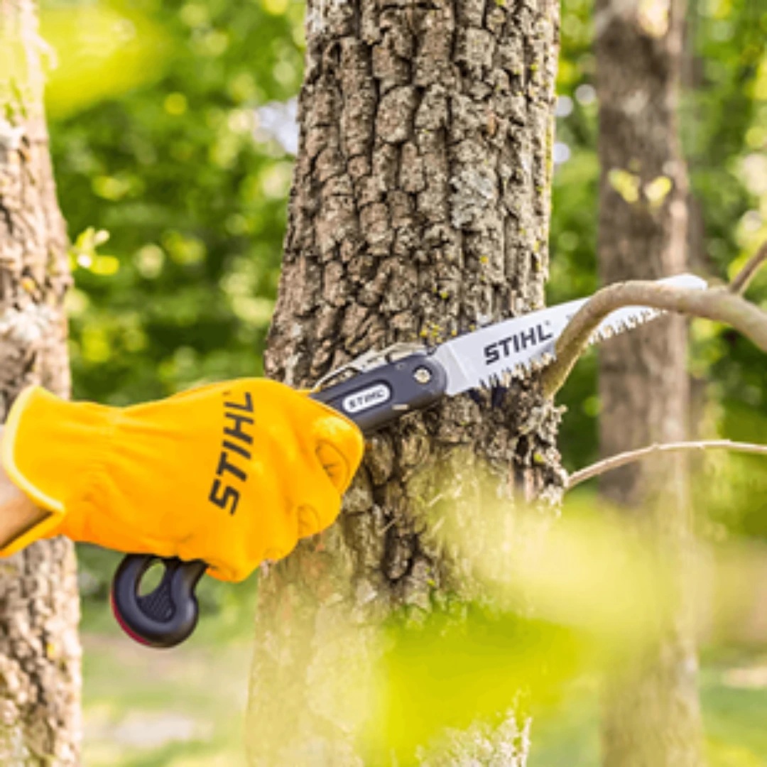 Handheld folding pruning saw with hard chrome-plated blade cutting a small tree branch in a garden setting