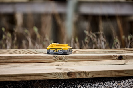 Yellow and gray DEWALT 20V XR POWERSTACK 5Ah battery resting on stacked wood boards for tools and home improvement tasks