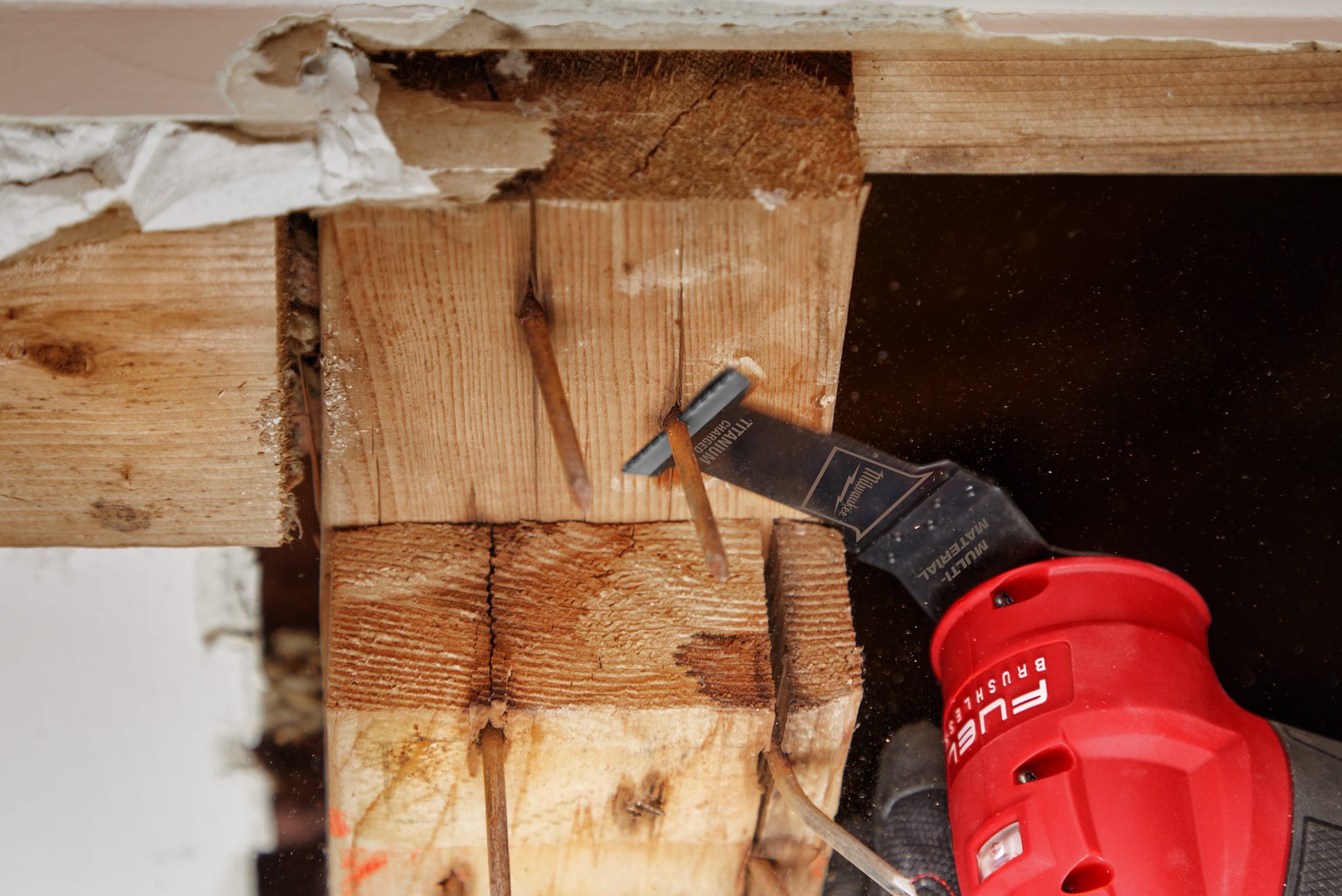 Multi-tool blade attached to red oscillating tool cutting through wood framing with embedded nails for home improvement tasks
