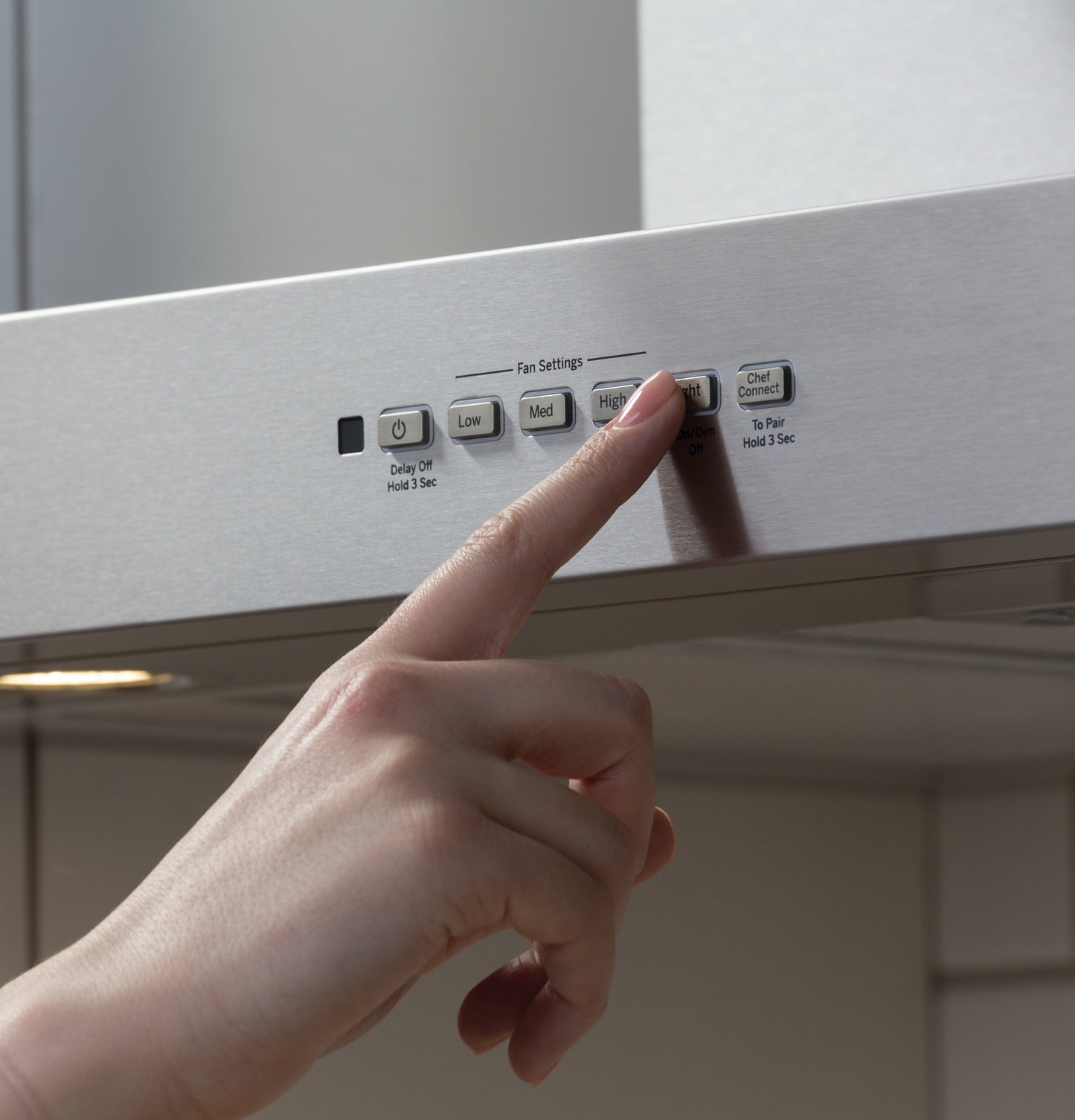 Hand pressing high-speed fan button on stainless steel wall mount range hood from kitchen appliances collection