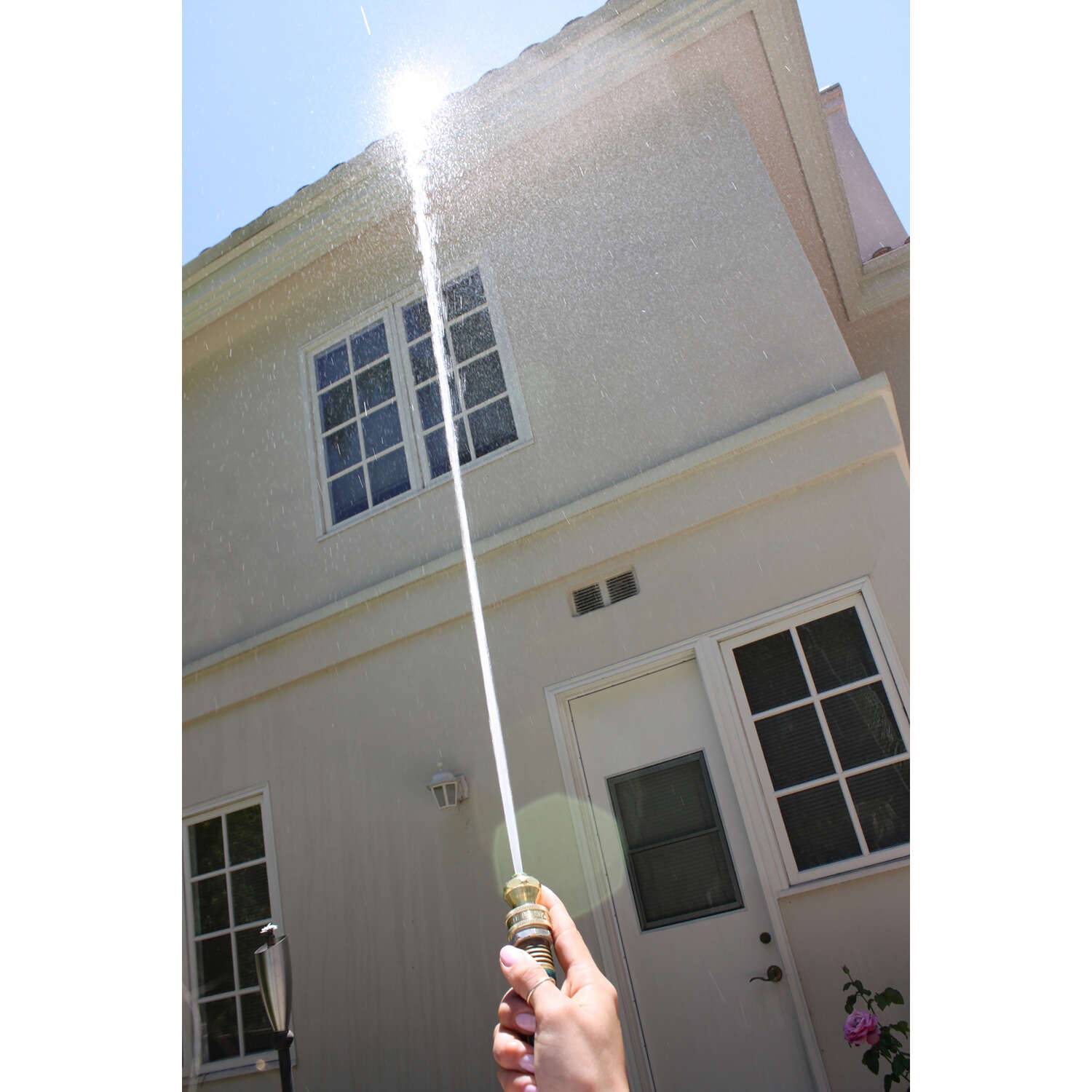 Hand holding brass twist nozzle spraying a powerful narrow stream of water for lawn and garden watering and irrigation