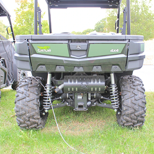 Rear view of a green utility vehicle with rugged suspension and large off-road tires on grass background