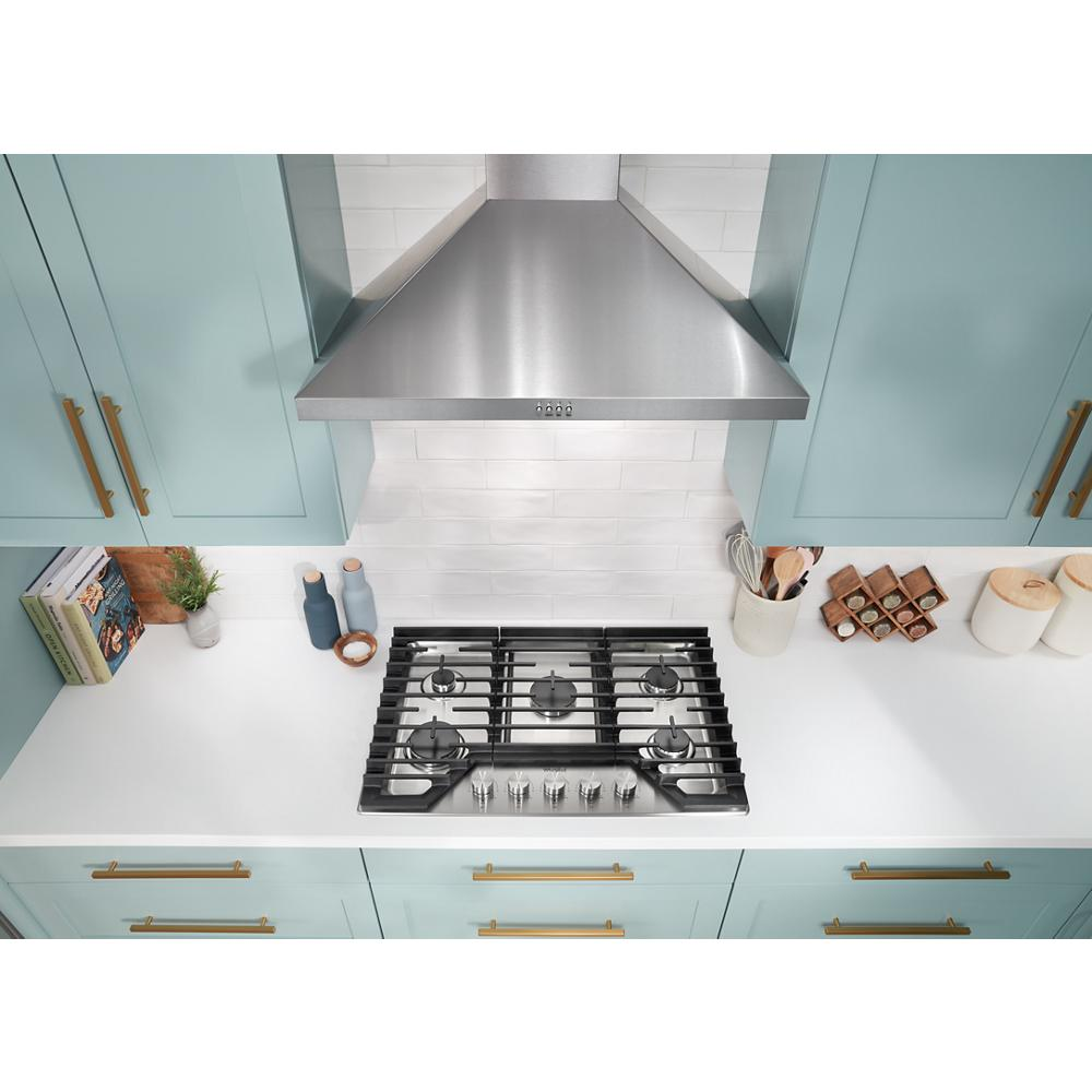 Top view of a modern 5-burner gas cooktop with hinged cast-iron grates in a kitchen with blue cabinetry and brass handles
